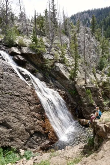 a girl perched on the cliff edge staring at the second waterfall on Fish Creek Trail which is one of the best things to do in Steamboat Springs