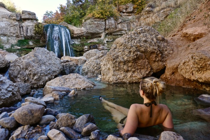 a girl soaking in a pool at fifth water hot springs staring at the waterfall