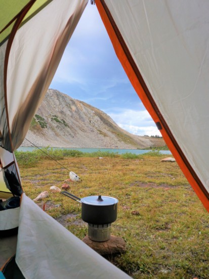 a backpacking campstove sitting outside a tent with a mountain in the distance