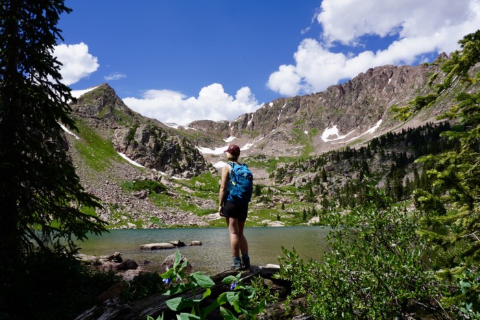 a girl with a hiking backpack in front of an alpine lake