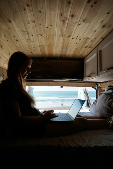 a girl working on her laptop in a van with a beach view using vanlife internet