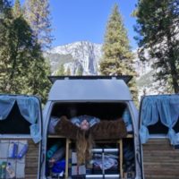 Emily hanging upside down from the bed in the van with El Capitan in the background