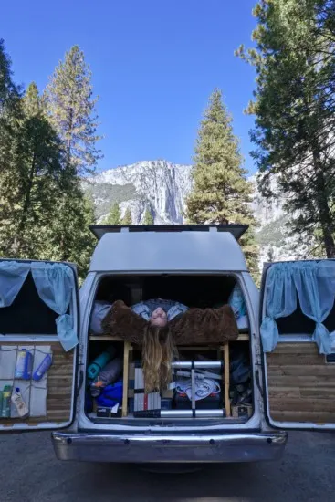 Emily hanging upside down from the bed in the van with El Capitan in the background
