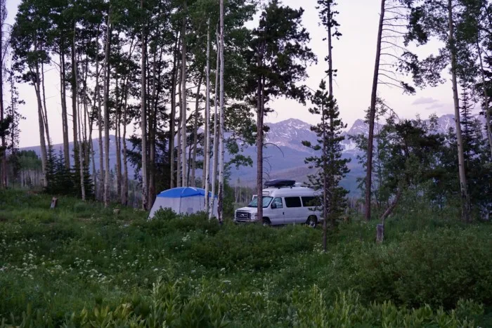 a van parked next to a tent with trees and mountains in the distance, showing an example of there is no limit to the length of travel if you like #vanlife full-time