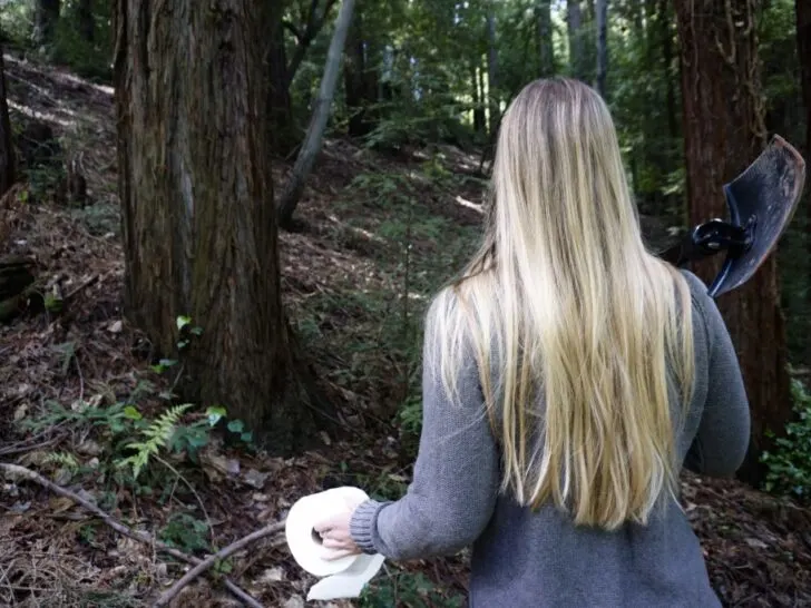 A girl holding a poop shovel and toilet paper in the forest