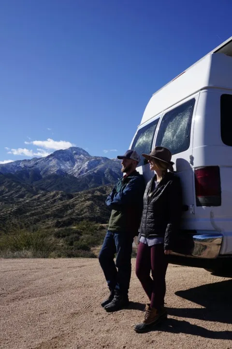 Jake and Emily leaning on their van, while looking out over the mountains