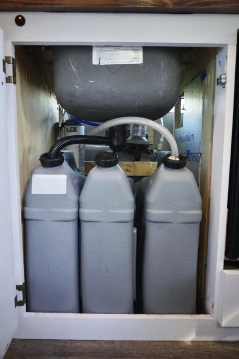 Three water storage jugs underneath the sink plumbing