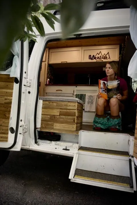 Emily sitting in the van on the bathroom cassette toilet reading a magazine looking out the doors