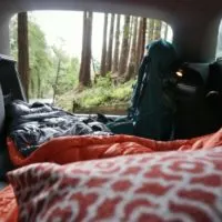 Car camping in a hatchback with a pillow and sleeping bag.