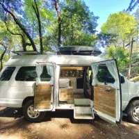 Two Roaming Souls Van with doors open showing the inside under bright green trees