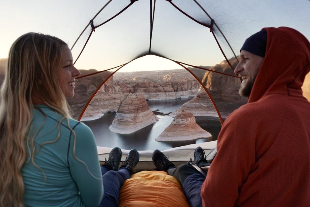 Jake and Emily smiling at each other with reflection canyon in the background peering through the tent door