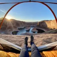 Emily with her feet out of the tent with a view of reflection canyon at sunrise