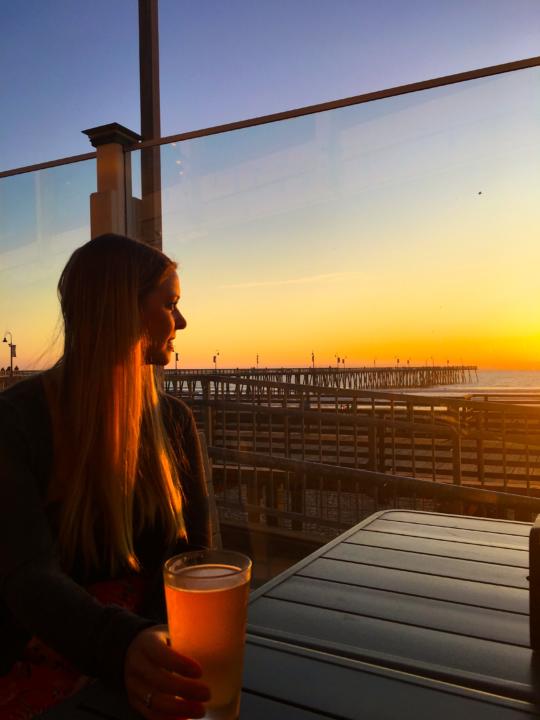 Emily staring out at the Pacific Ocean with a beer at sunset at Wooly's in Pismo Beach