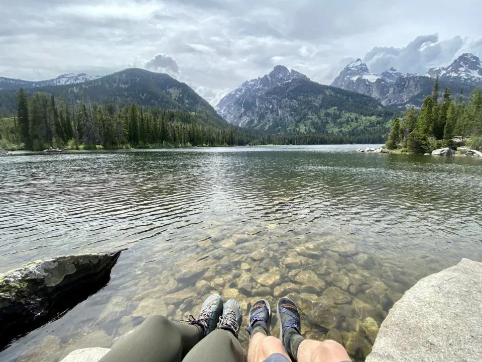 Jake and Emily dangling their feet over Taggert Lake with the Tetons in the background