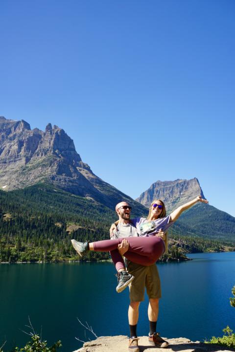 Emily in Jakes arms with St. Mary's Lake in the background showing the epic peaks and aqua blue water