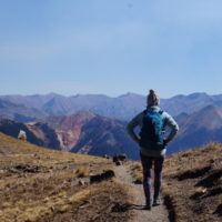 Emily hiking back down Columbine Lake Trail with red mountain peaks in the distance