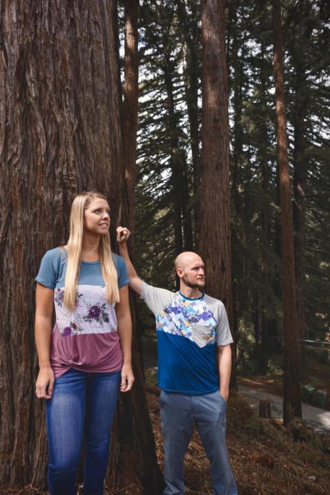 Jake and Emily posing against a redwood tree with The Woods Clothing T Shirt, which can make a great custom vanlife gift idea