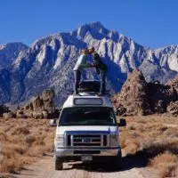 Jake and Emily kissing on top of the van with Inyo Mountains and Alabama Hills in the background