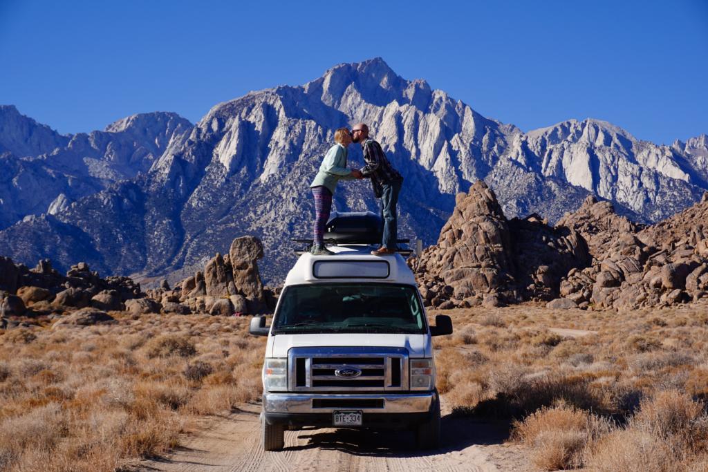 Jake and Emily kissing on top of the van with Inyo Mountains and Alabama Hills in the background