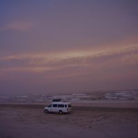 A couple vans driving on the beach, debating the merits of 2wd vs 4wd on a beach.