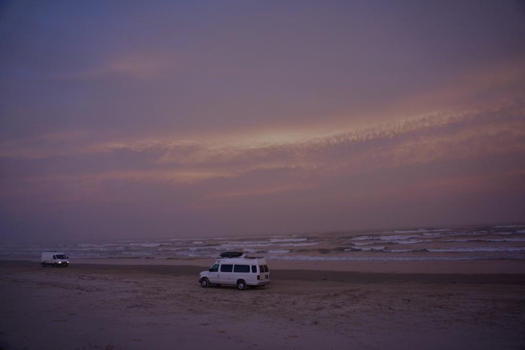 A couple vans driving on the beach, debating the merits of 2wd vs 4wd on a beach.