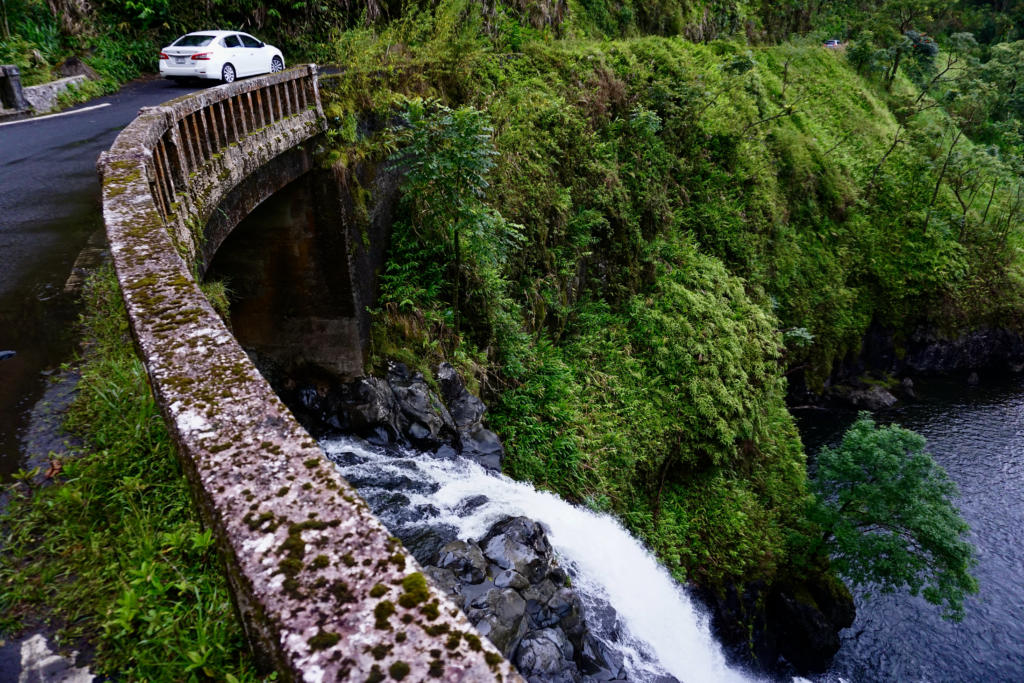 Looking over a one-lane bridge at a waterfall on the Road To Hana