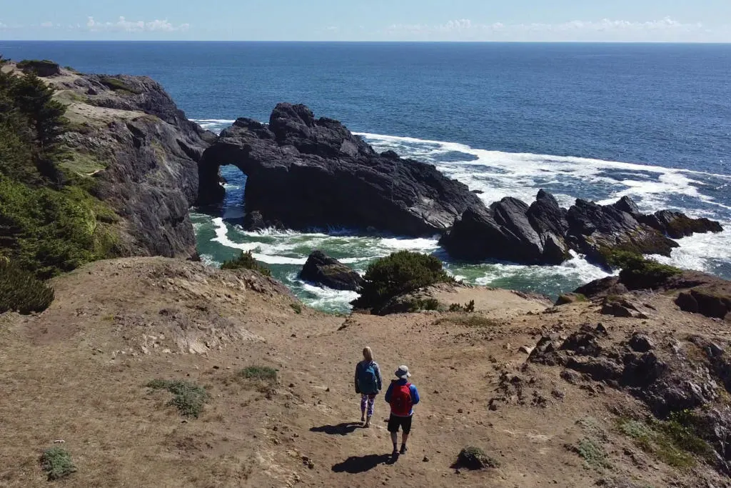 A drone photo of the Two Roaming Souls hiking on Indian Sands Trail, looking down at the natural rock arch.