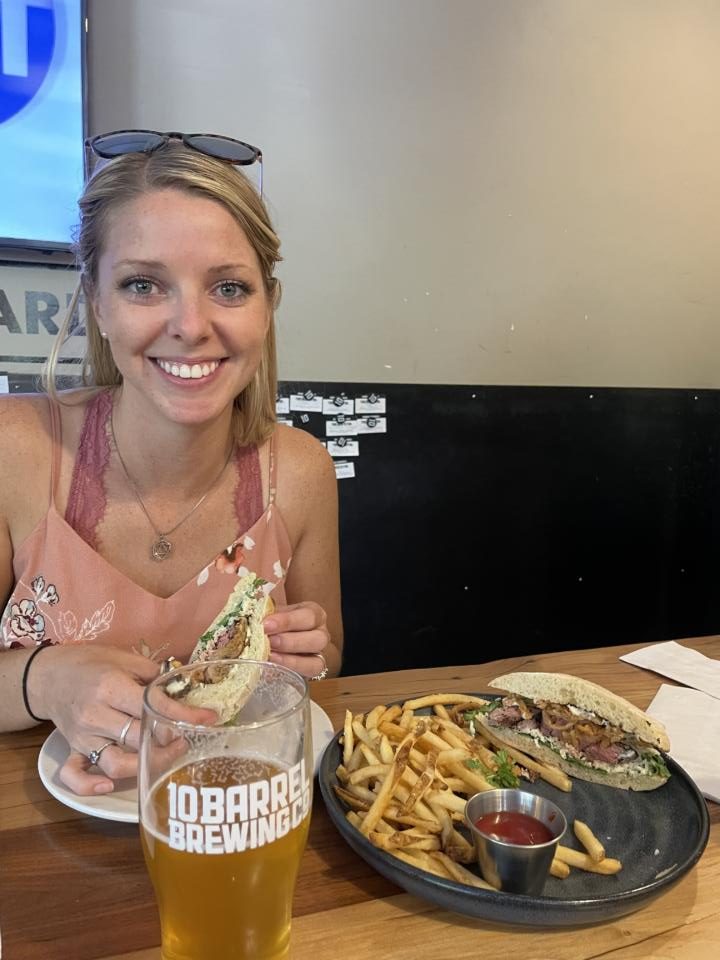 Emily holding a steak sandwich w/ a beer at10 Barrel Brewing which was a restaurant style brewery on our self-guided brewery tour in Bend, Oregon