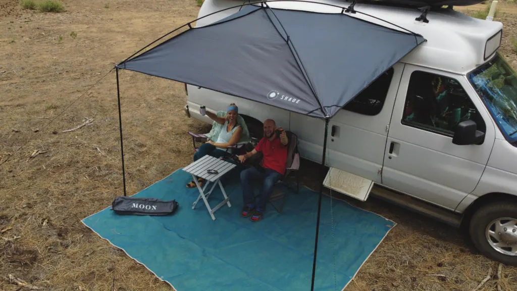 The Two Roaming Souls cheers some drinks under the Moon Shade and CGear Sand-Free Mat Patio for their campervan.