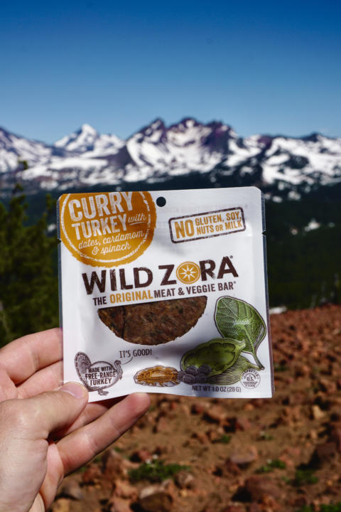 Jake holding the Curry Turkey Wild Zora Meat & Veggie Bar with mountains in the background