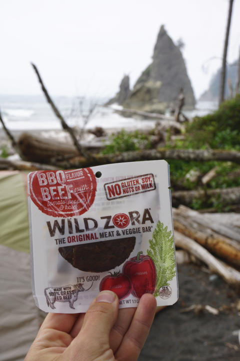 Jake holding the BBQ Beef Wild Zora Meat & Veggie Bar with Rialto Beach in the background