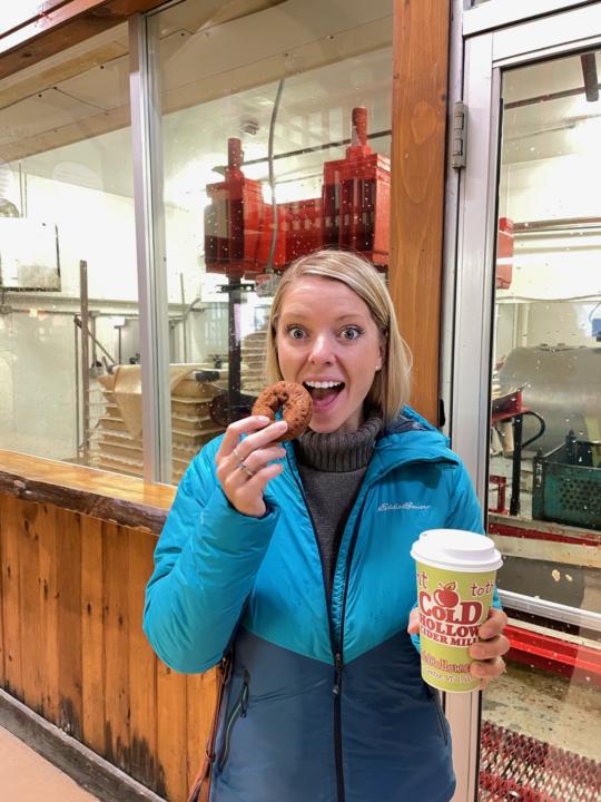 emily eating a donut with a cider in hand from Cold Hollow Cider Mill in Stowe, VT