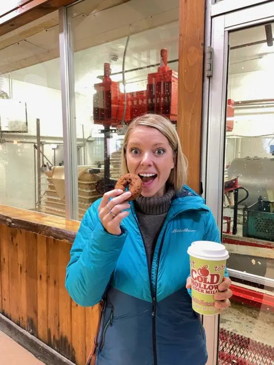 emily eating a donut with a cider in hand from Cold Hollow Cider Mill in Stowe, VT