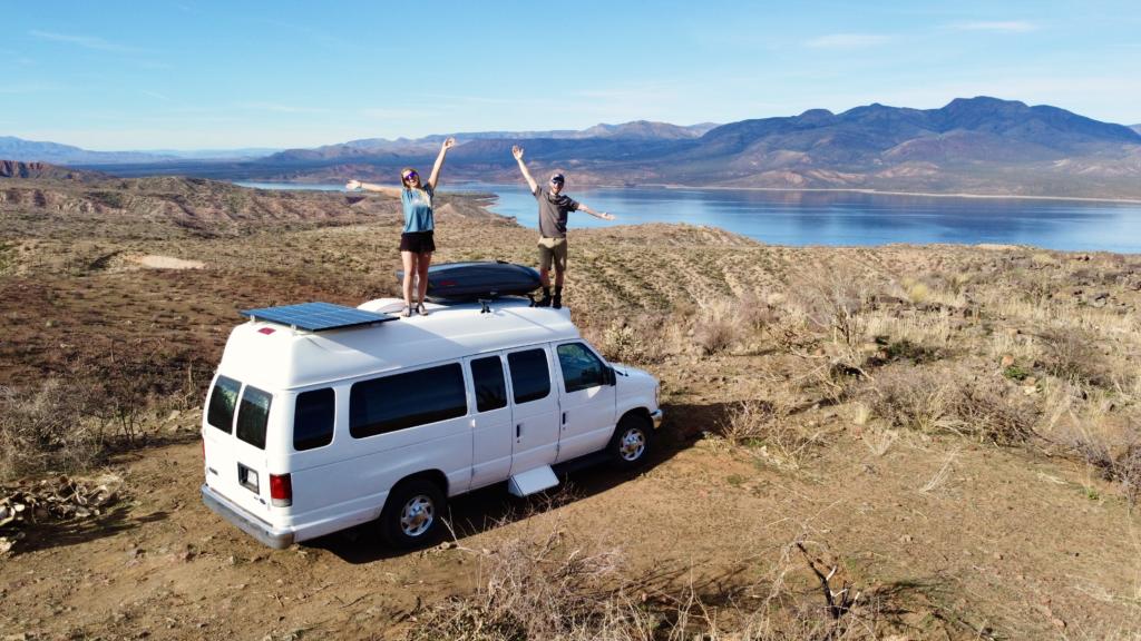 jake and emily standing on their van with Lake Roosevelt in the distance which is one of the best campsites in the western U.S.