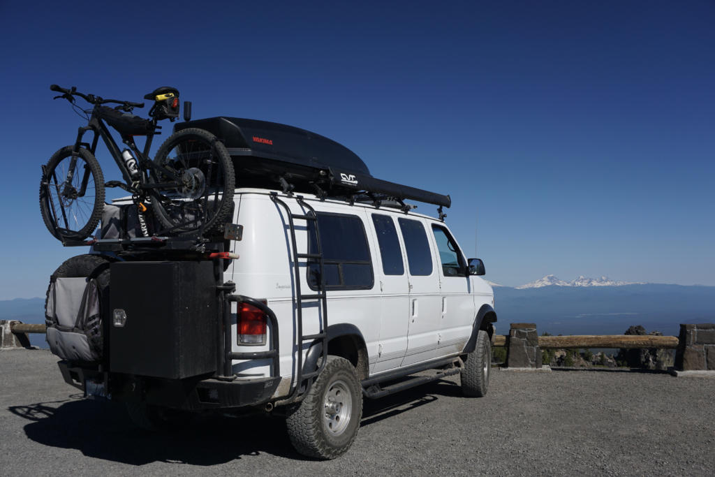 A low-roof Ford campervan with bikes and a ski box.