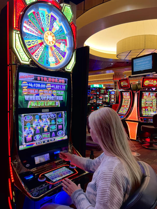 Emily playing a Wheel Of Fortune slot machine on the Sky Ute Casino Floor.