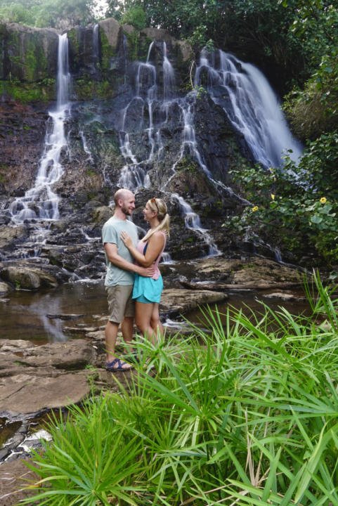 a couple posing in front of a long exposure of Hoopii Waterfall which is one of the best hikes in Kauai