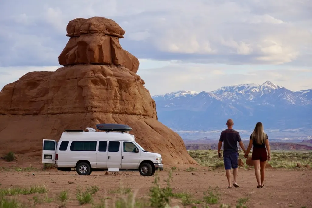 a couple walking toward their campervan with a hoodoo and the Henry Mountains in the background