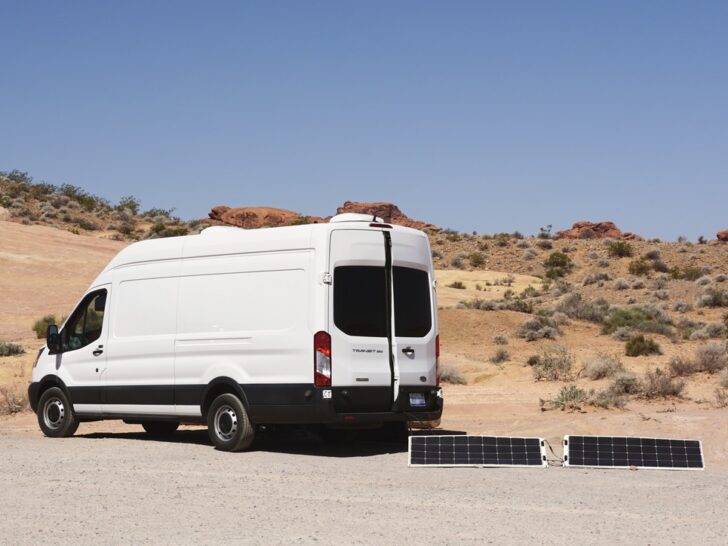 A white Ford Transit campervan with portable solar panels.