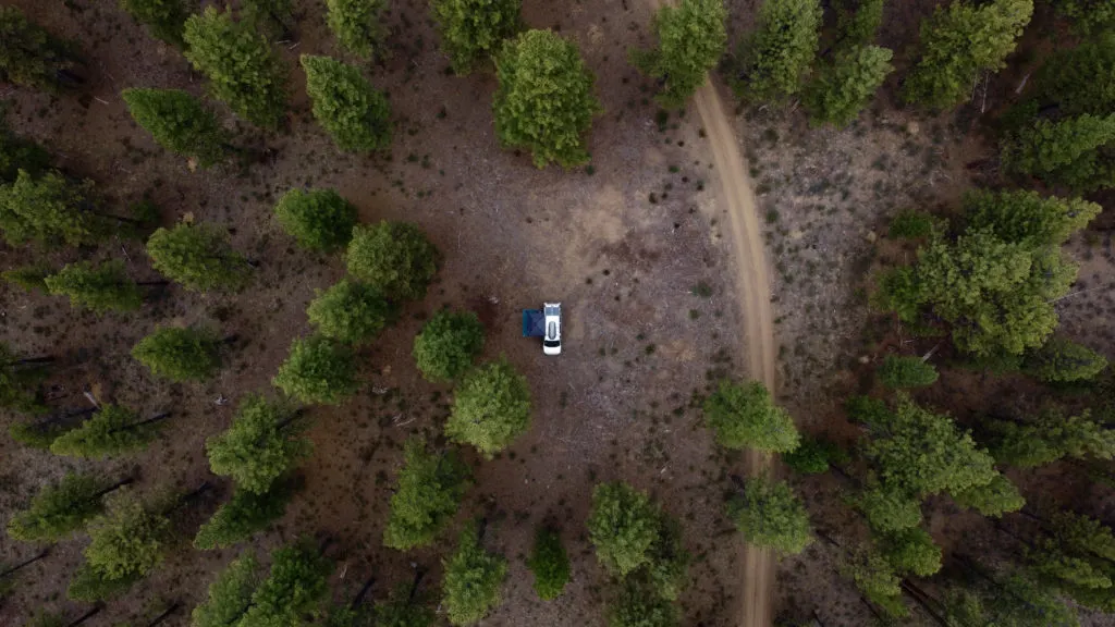 Overhead shot of a forest out west with a lonely campervan at a campsite.