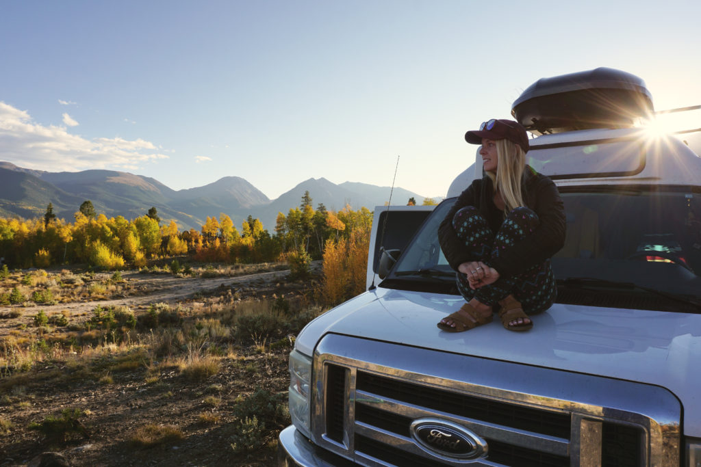 Emily sitting on our campervan with fall colors and mountains in the background.
