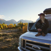 Emily sitting on our campervan with fall colors and mountains in the background.