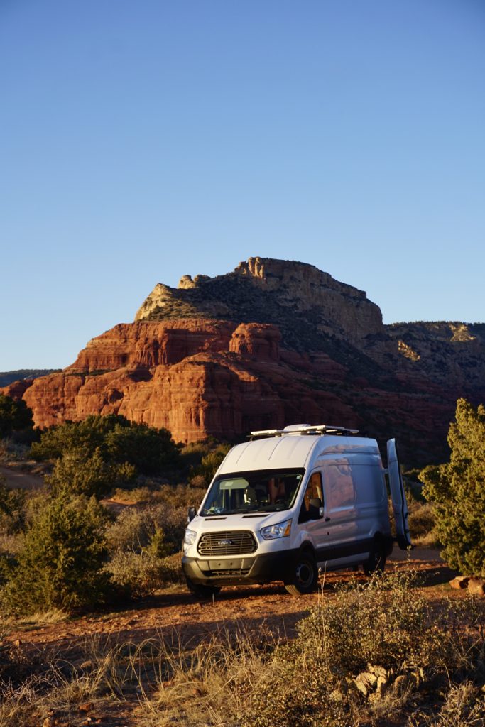 A high-roof white Ford Transit Campervan parked in the red rocks of Sedona.