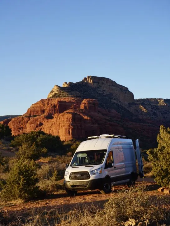 A high-roof white Ford Transit Campervan parked in the red rocks of Sedona.