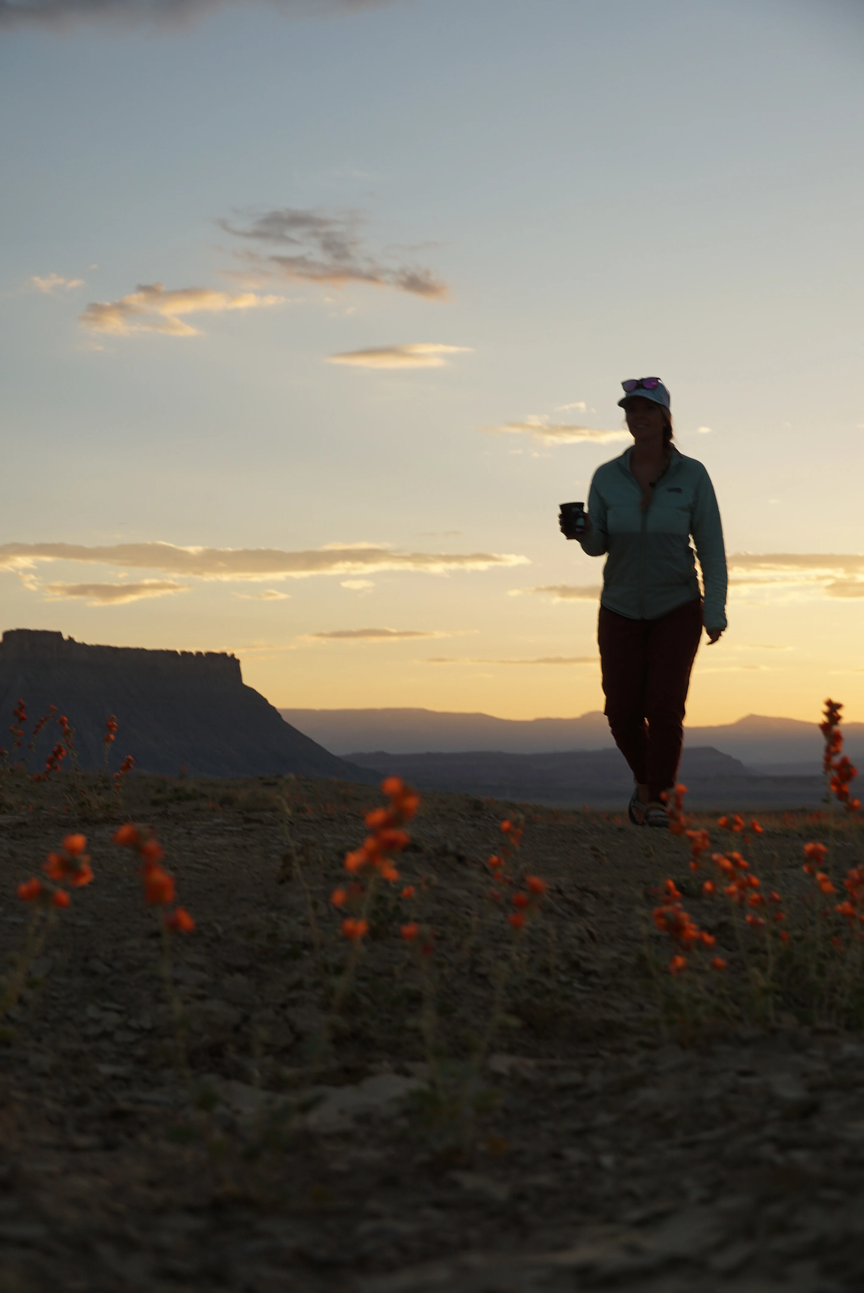 walking along skyline view at Moonscape overlook, a girl walking at sunset with orange wildflowers and factory butte in the distance