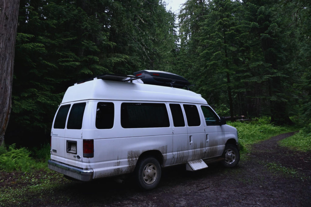 A Campervan parked in a dark and dreary forest.