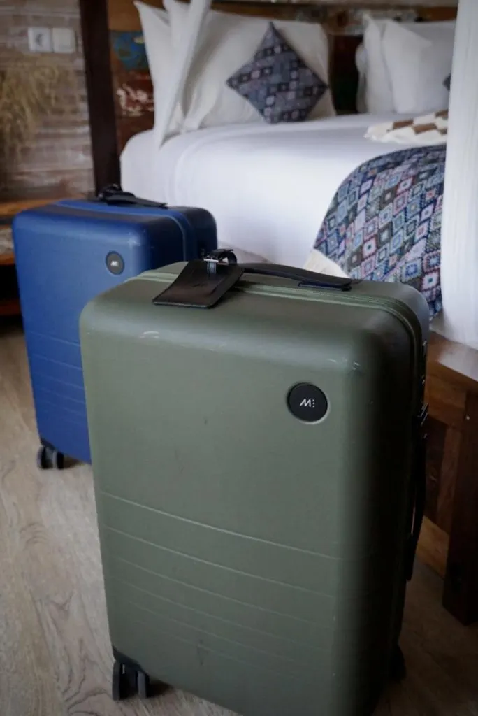 Blue & Green Monos Carry On Plus in front of a hotel bed