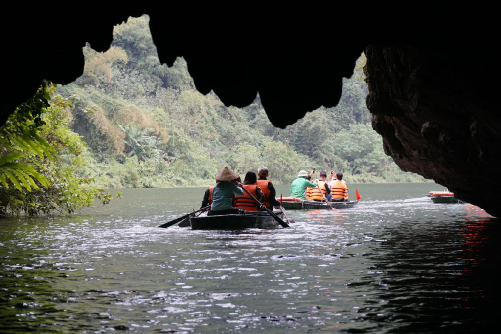 Boat Rower going under a cave using their hands to paddle on the Trang An Boat Tour