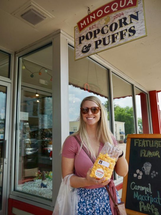 Emily standing under the Minocqua Popcorn Company with cheesy popcorn in hand, which is one of the best things to do in Minocqua