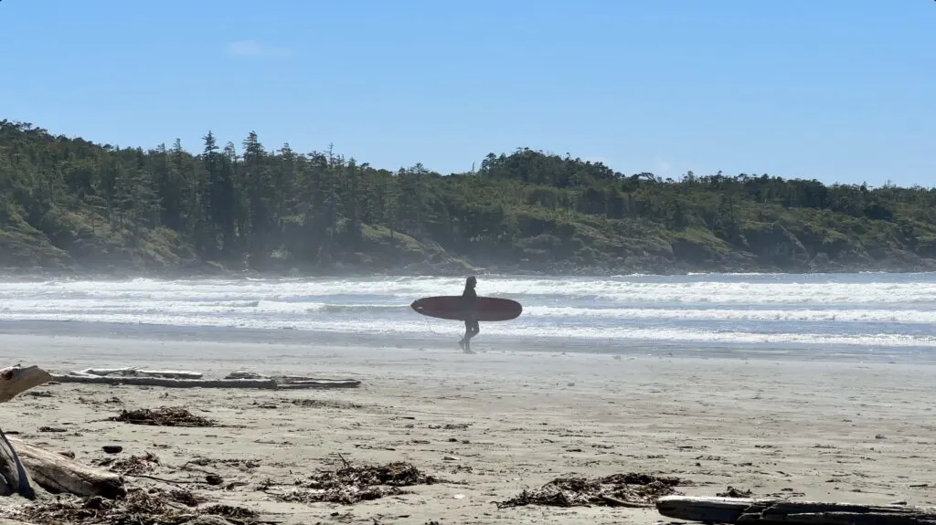 a surfer walking toward the ocean at Cox Bay Beach